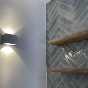 Detailansicht von Fliesenwand, Holzregalen und Wandleuchte